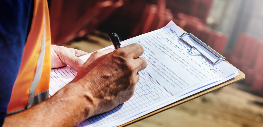 Rzeczoznawca maszyn budowlanych w kamizelce odblaskowej wypełniający formularz wyceny na placu budowy – wycena maszyn budowlanych. Rzeczoznawca maszyn budowlanych w kamizelce odblaskowej wypełniający formularz wyceny na placu budowy – wycena maszyn budowlanych.